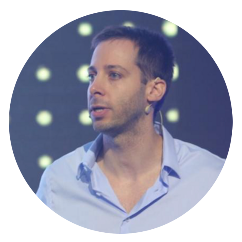 Man wearing a light blue shirt, talking on stage.